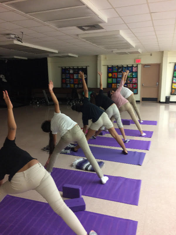 Students in A4L's after-school program with Susana Saumell at Feinberg Fisher K-8 Center practice triangle pose pose.