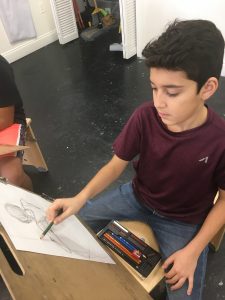 Middle school boy drawing with pencil on paper.